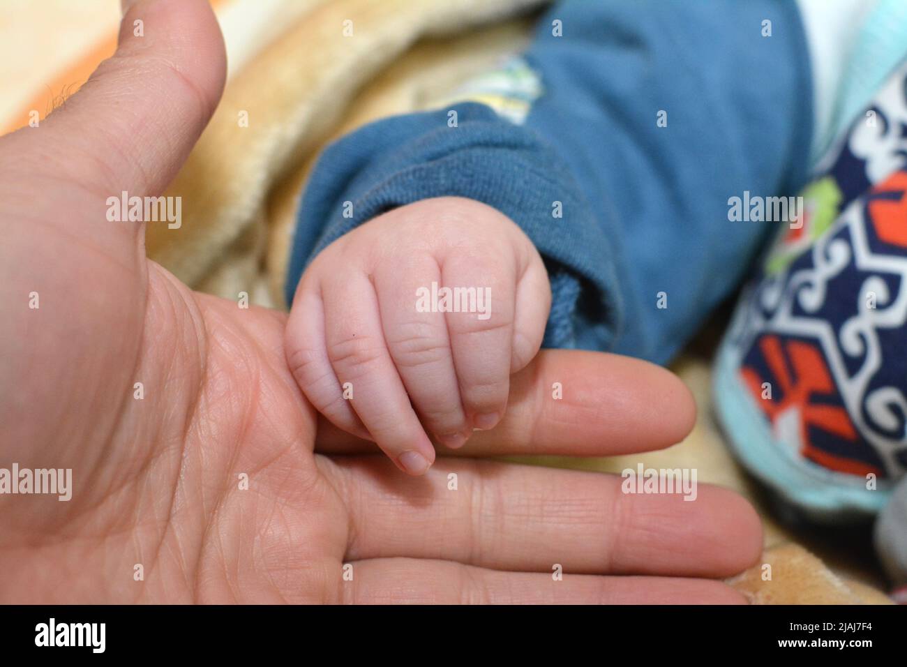 La mano di un neonato in mano di papà su uno sfondo sfocato, primo piano neonato che tiene la mano di suo padre, amore famiglia assistenza sanitaria e medico Foto Stock