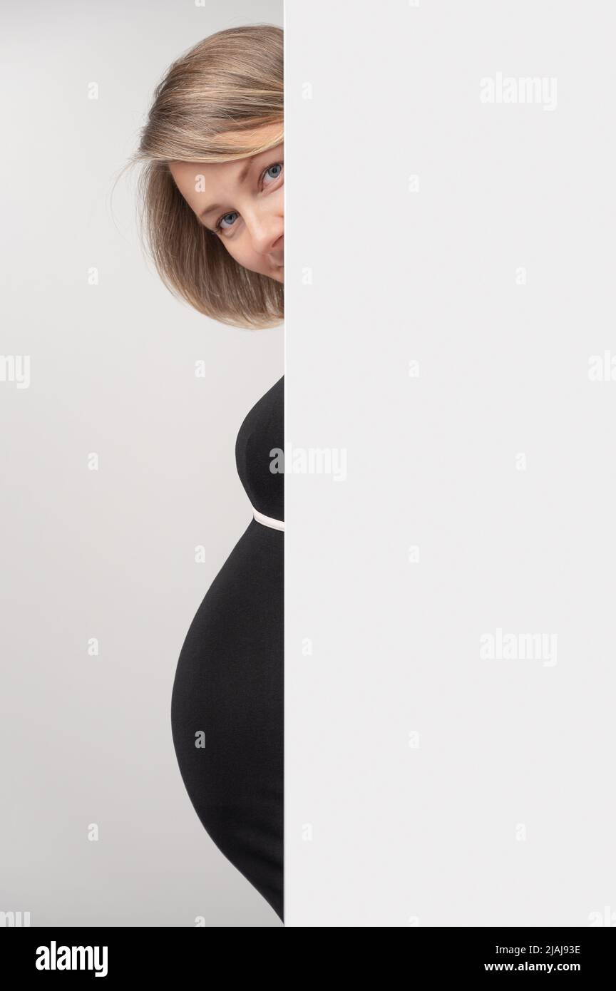 Donna incinta che sbucciava dalla parete bianca. Donna incinta felice dietro la lavagna bianca per la pubblicità del testo. Foto Stock