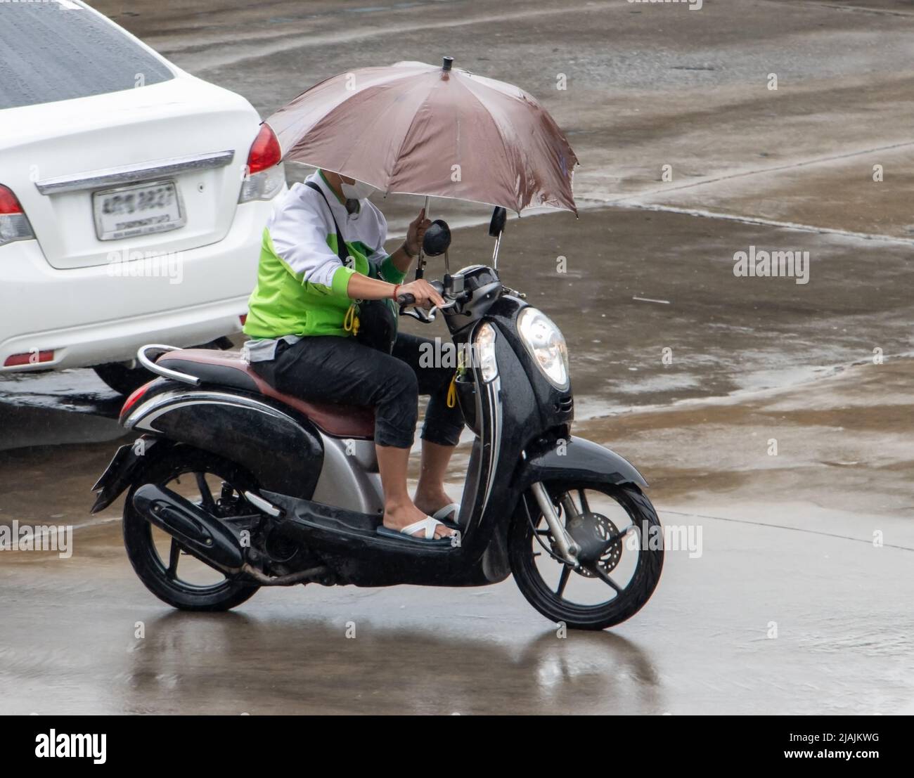 Un motociclista guida una moto con ombrello in una mano Foto Stock