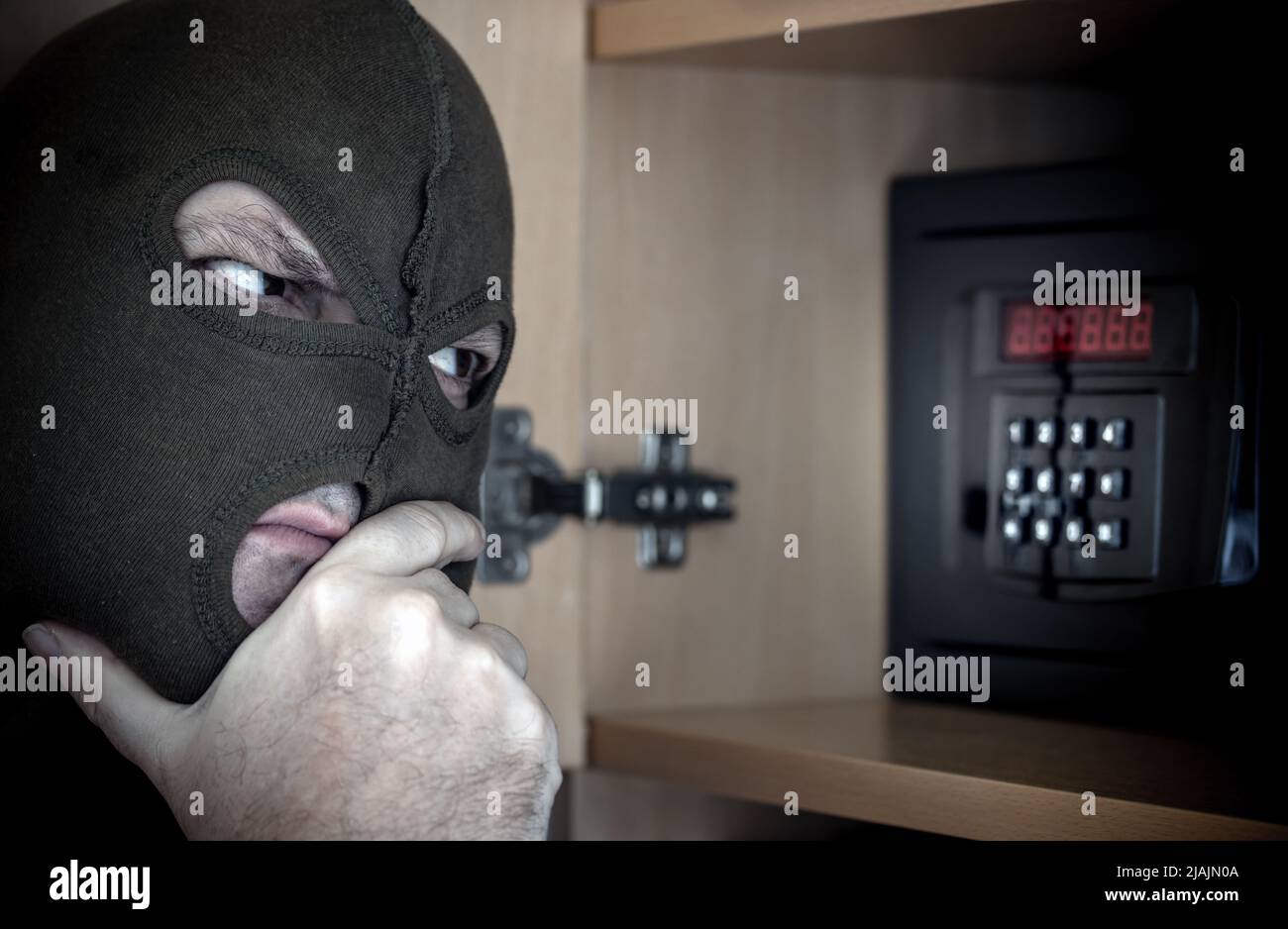 Il criminale con balaclava pensa al codice per la sicurezza chiusa a chiave Foto Stock