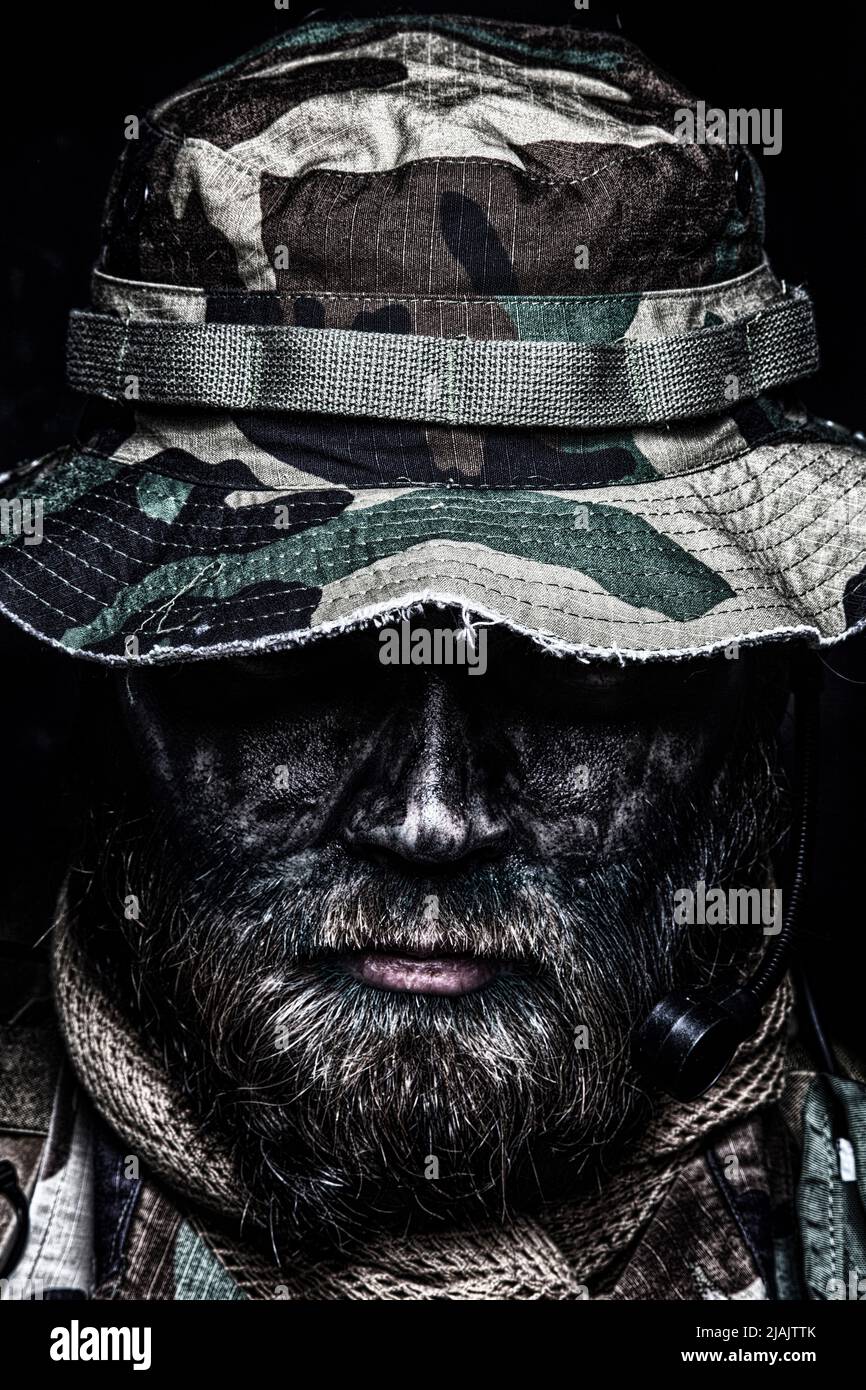 Primo piano ritratto di un comandante beardo combattente in boonie cappello e camouflage viso vernice. Foto Stock