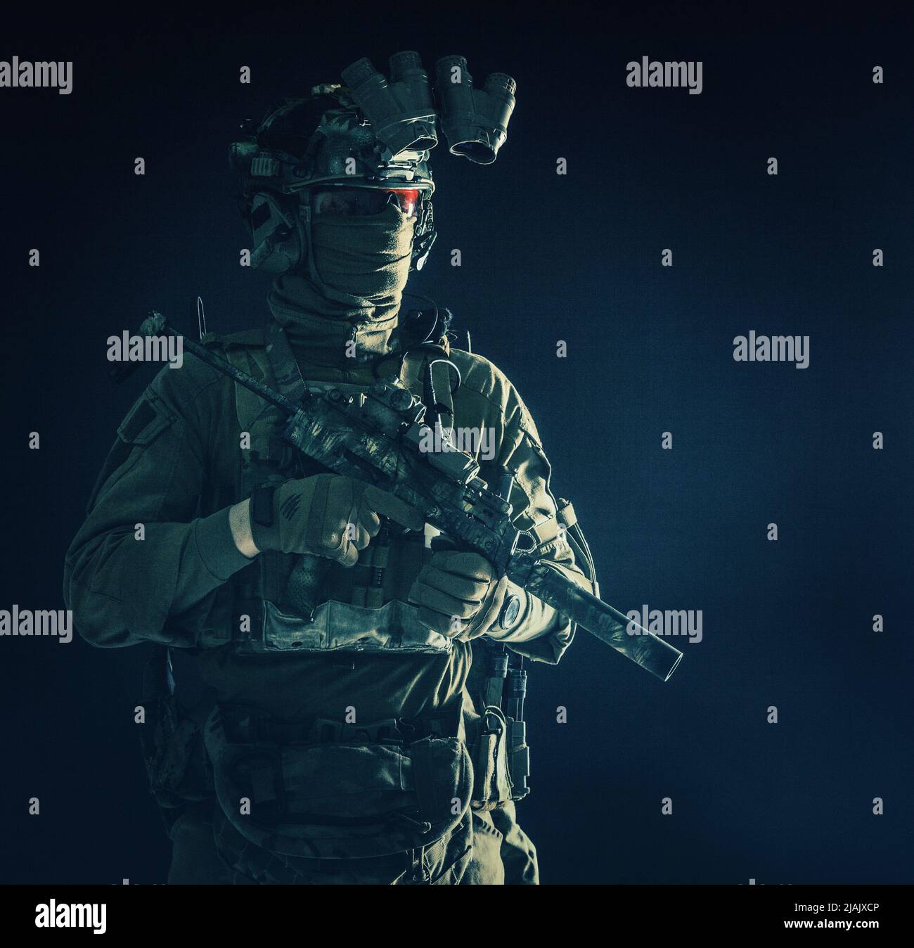 Un combattente d'elite in piedi nel buio con mini mitragliatrice e dispositivo di visione notturna. Foto Stock
