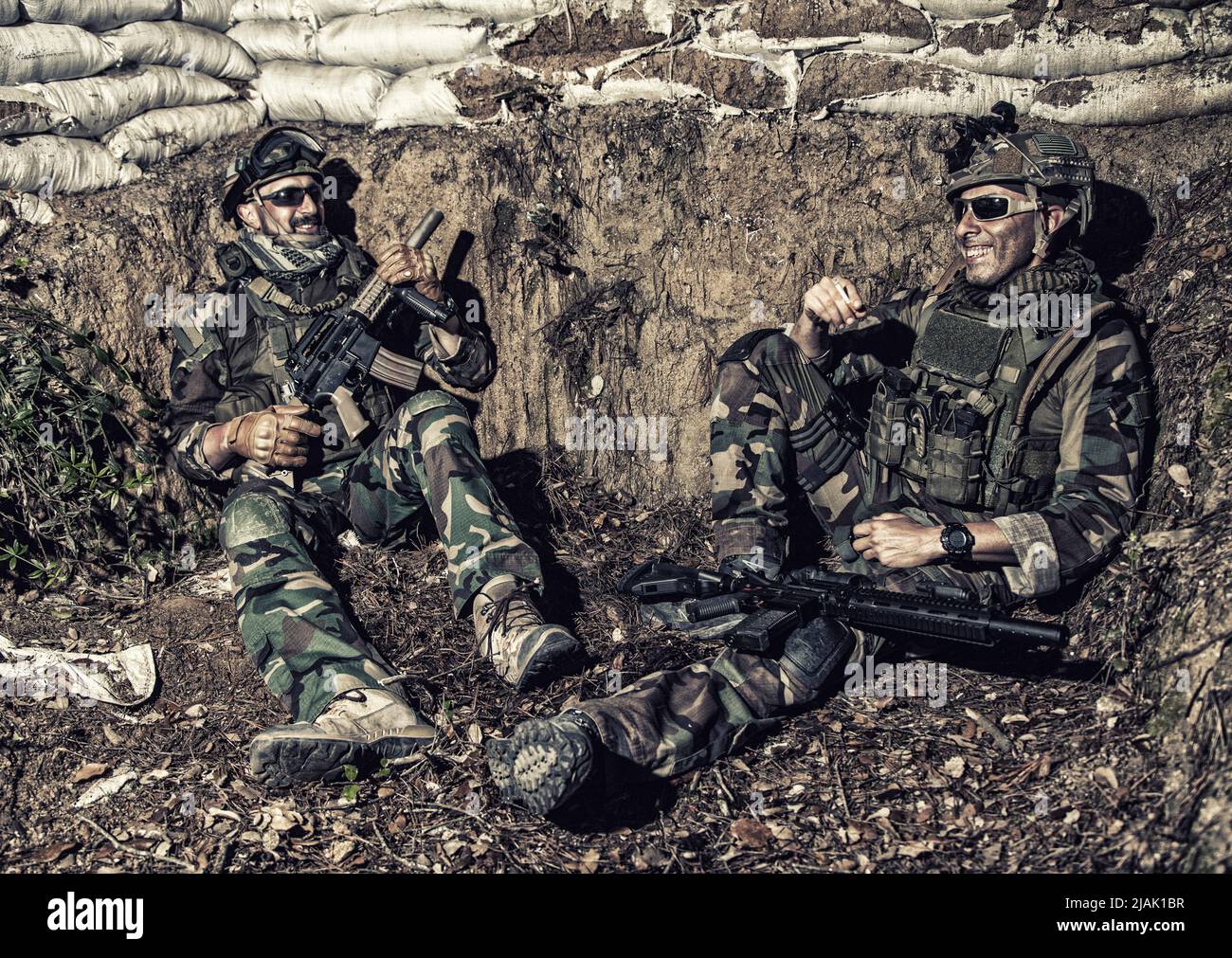 Combattenti armati di commando seduti in una trincea di notte, parlando e raccontando battute. Foto Stock