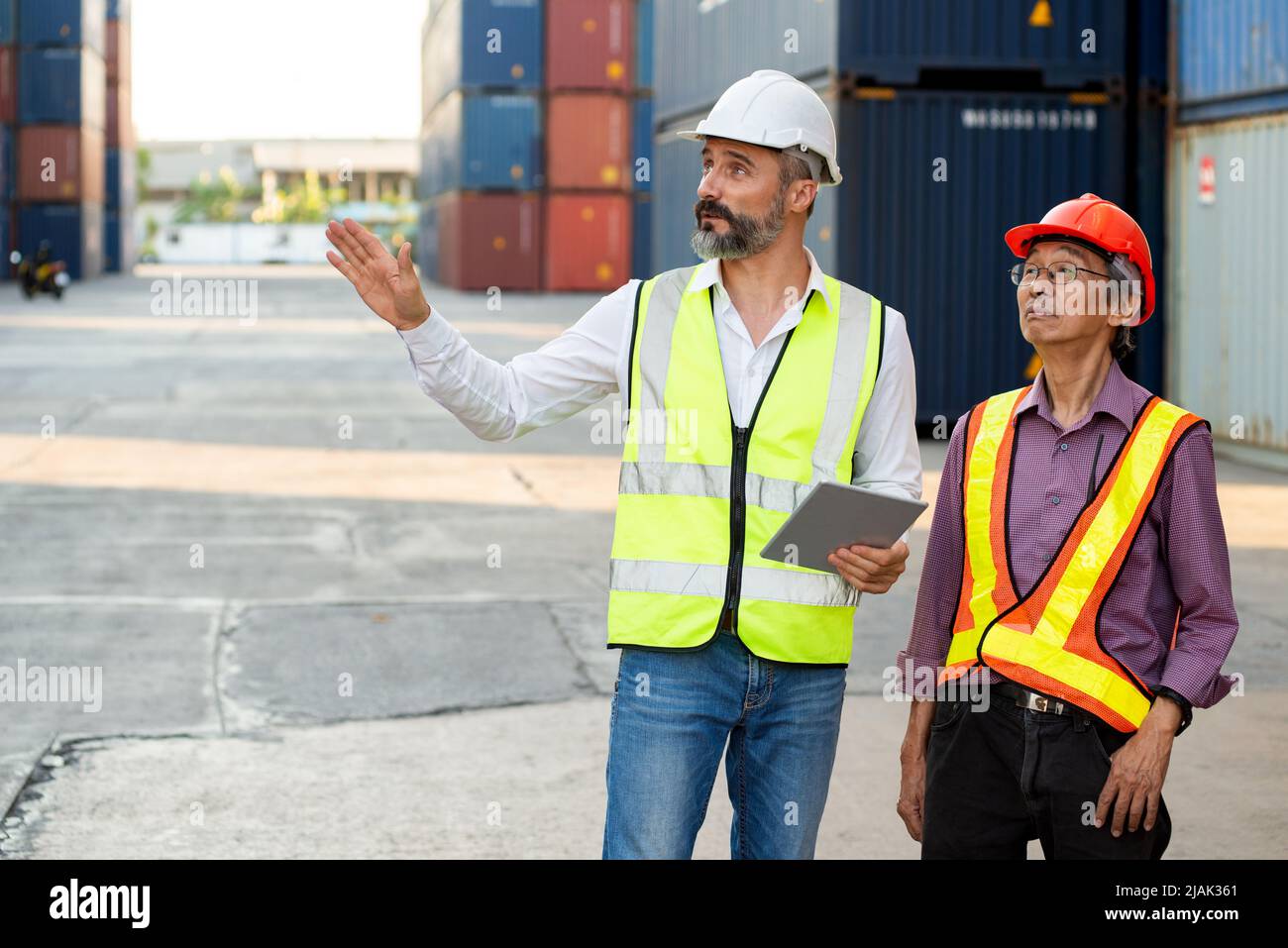 Il responsabile maschio caucasico e l'ingegnere senior utilizzano il tablet per controllare l'importazione di container di merci da esportazione che caricano nel magazzino di distribuzione. Foto Stock