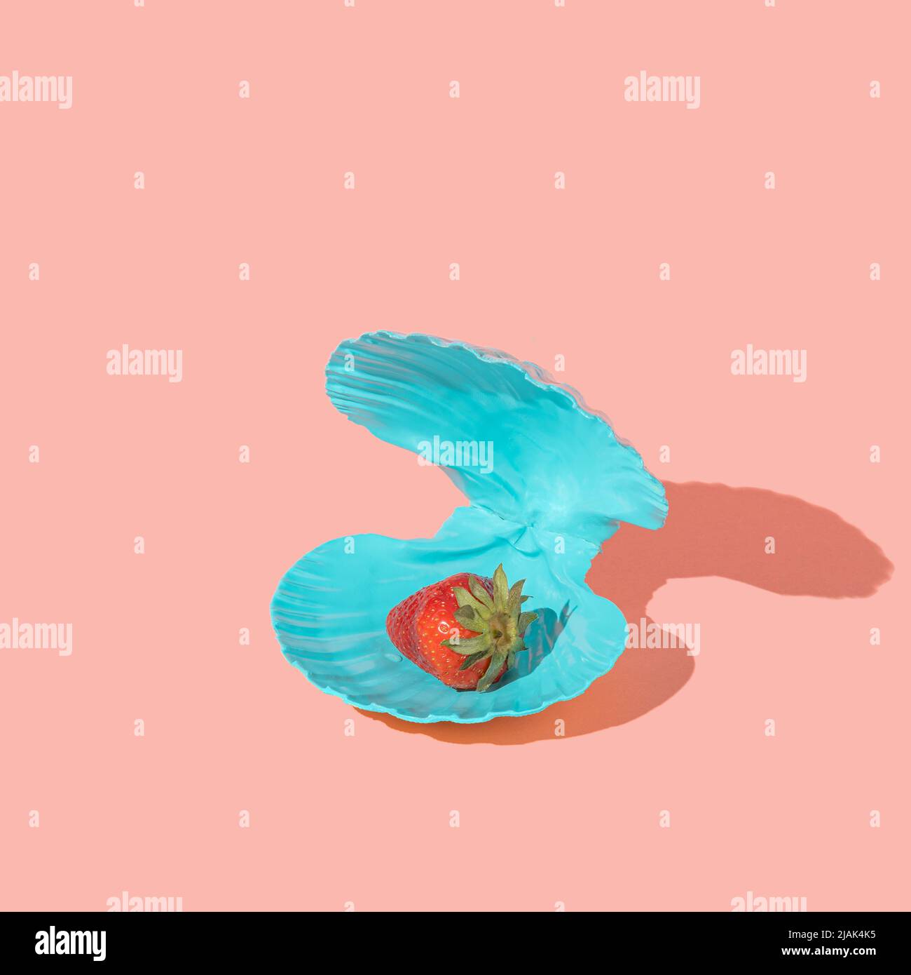 Fragola in una conchiglia blu invece di perla su sfondo rosa. Estate minimo sano concetto di cibo. Layout isometrico. Quadrato con spazio di copia Foto Stock