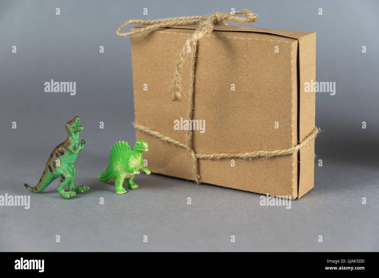 Scatola di cartone marrone e miniature di due dinosauri su sfondo grigio. Piccole figure verdi di animali di preda in piedi sulle loro zampe posteriori. Reg Foto Stock