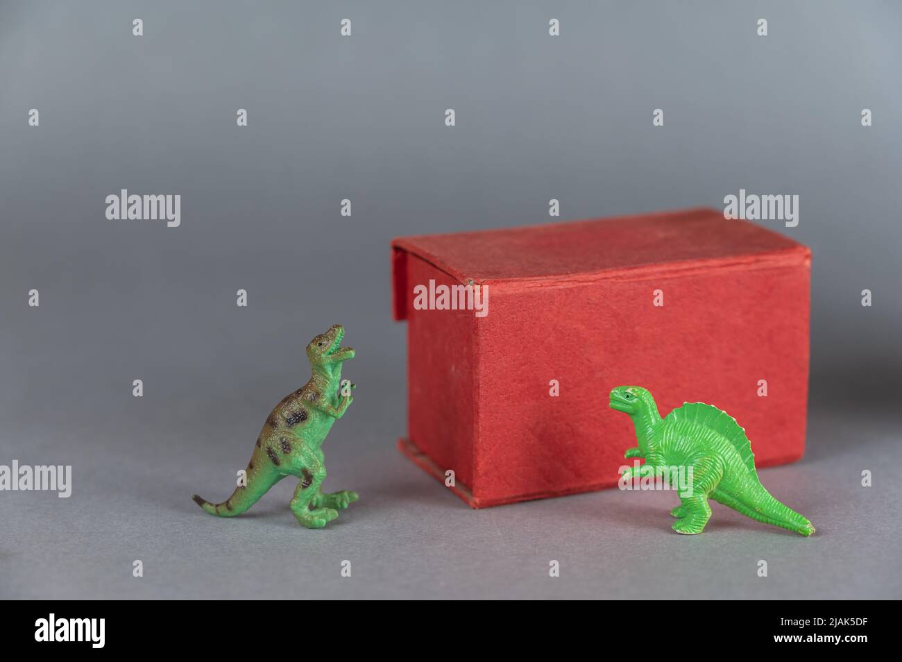 Scatola rossa e miniature di due dinosauri su sfondo grigio. Piccole figure verdi di animali di preda in piedi sulle loro zampe posteriori. Clo rettangolare Foto Stock