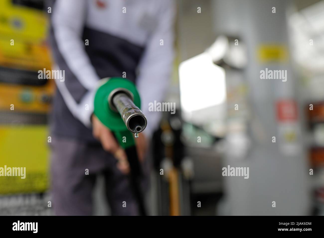 Profondità di campo bassa (fuoco selettivo) dettagli con un uomo che tiene una pompa carburante gocciola di benzina in una stazione di servizio. Foto Stock