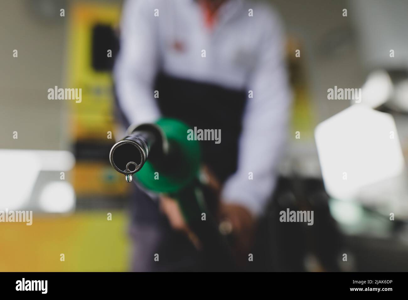 Profondità di campo bassa (fuoco selettivo) dettagli con un uomo che tiene una pompa carburante gocciola di benzina in una stazione di servizio. Foto Stock