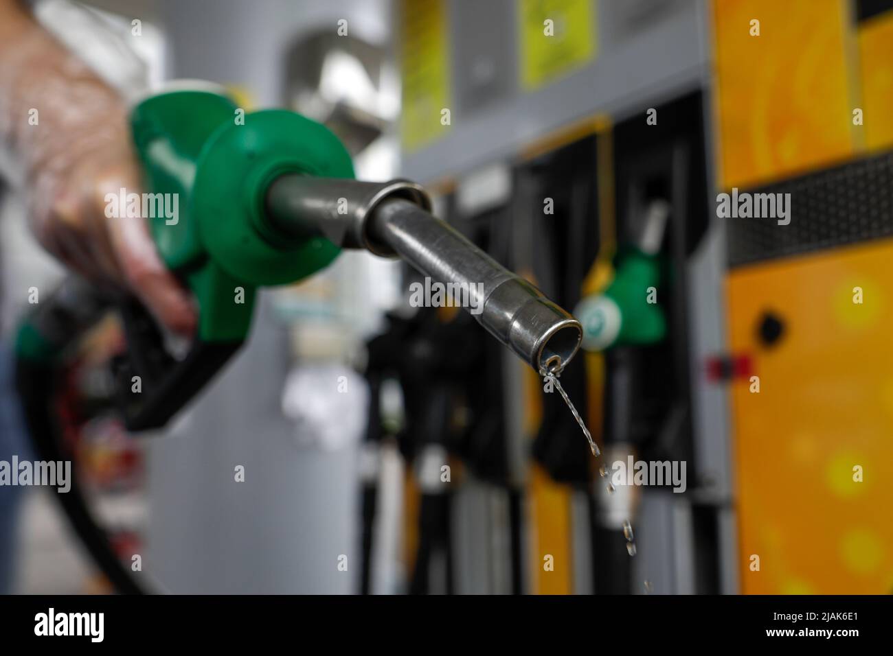 Profondità di campo bassa (fuoco selettivo) dettagli con un uomo che tiene una pompa carburante gocciola di benzina in una stazione di servizio. Foto Stock