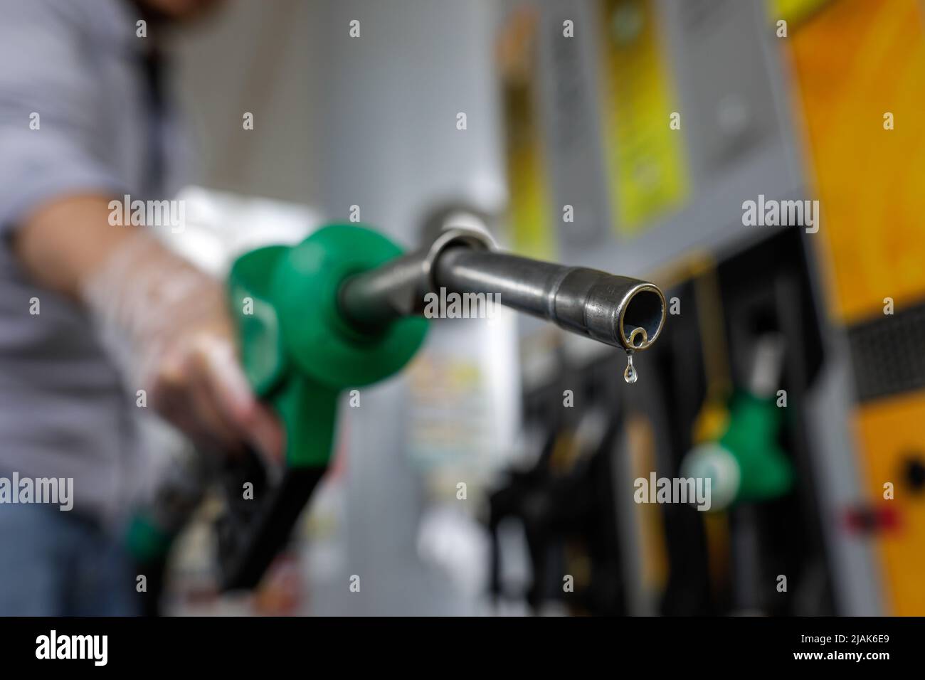 Profondità di campo bassa (fuoco selettivo) dettagli con un uomo che tiene una pompa carburante gocciola di benzina in una stazione di servizio. Foto Stock