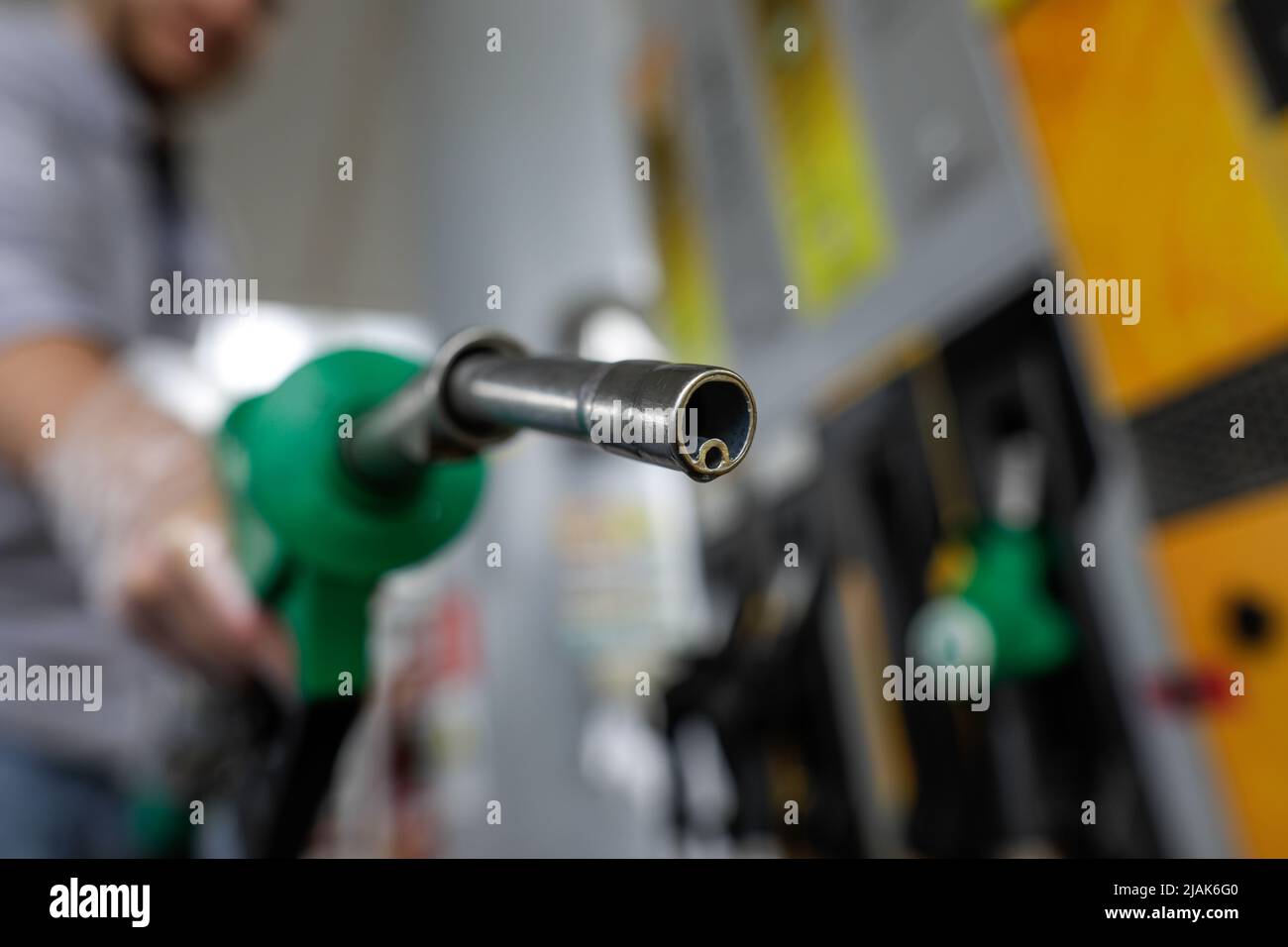 Profondità di campo bassa (fuoco selettivo) dettagli con un uomo che tiene una pompa carburante gocciola di benzina in una stazione di servizio. Foto Stock