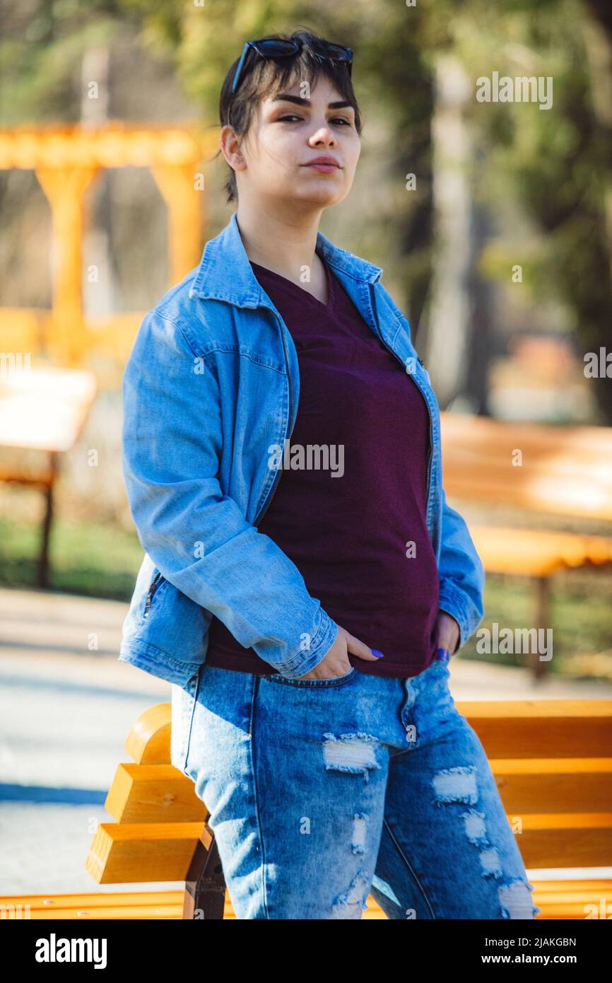 Bella ragazza con corti capelli neri nel suo 20s nel parco che indossa jeans blu chiaro e una giacca di denim blu chiaro Foto Stock