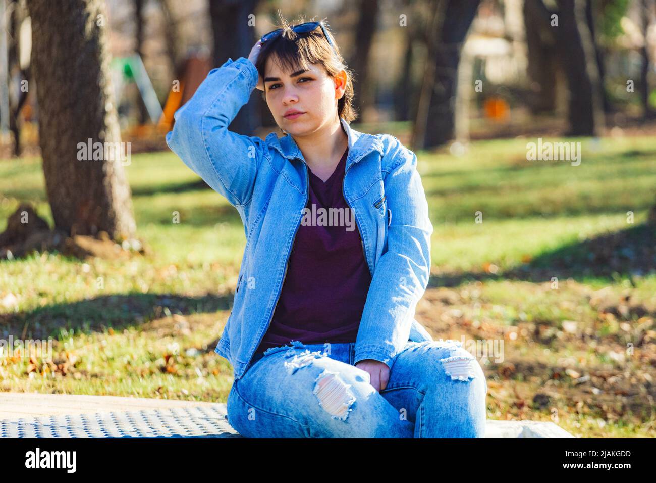 Bella ragazza con corti capelli neri nel suo 20s nel parco che indossa jeans blu chiaro e una giacca di denim blu chiaro Foto Stock