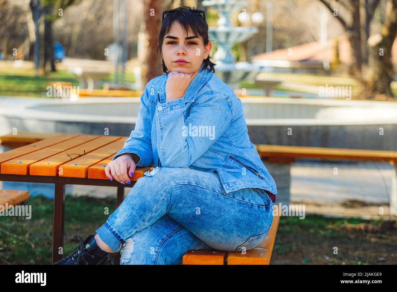 Bella ragazza con corti capelli neri nel suo 20s nel parco che indossa jeans blu chiaro e una giacca di denim blu chiaro Foto Stock