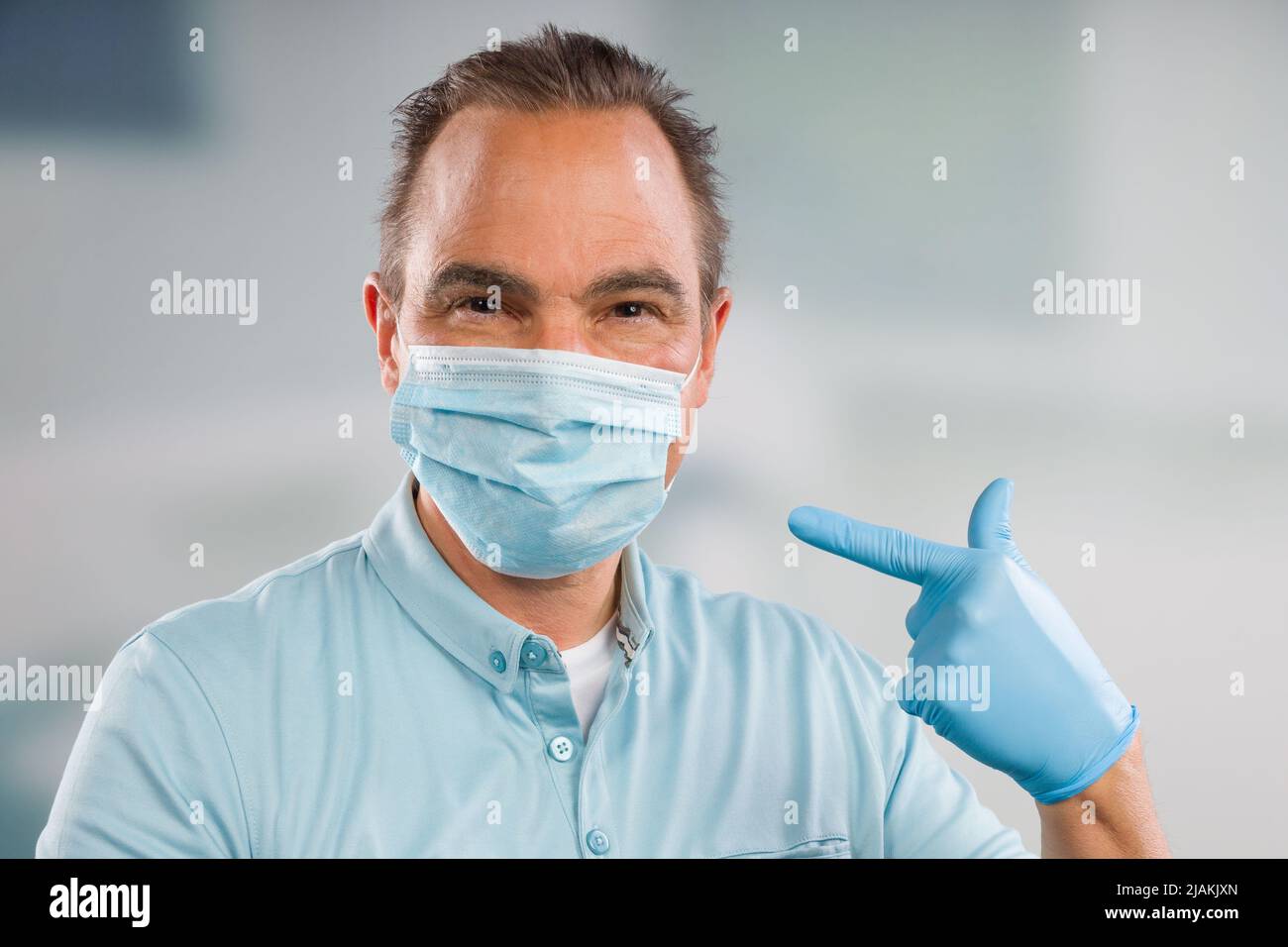 Medico con maschera medica e guanti medici punta alla sua maschera facciale Foto Stock