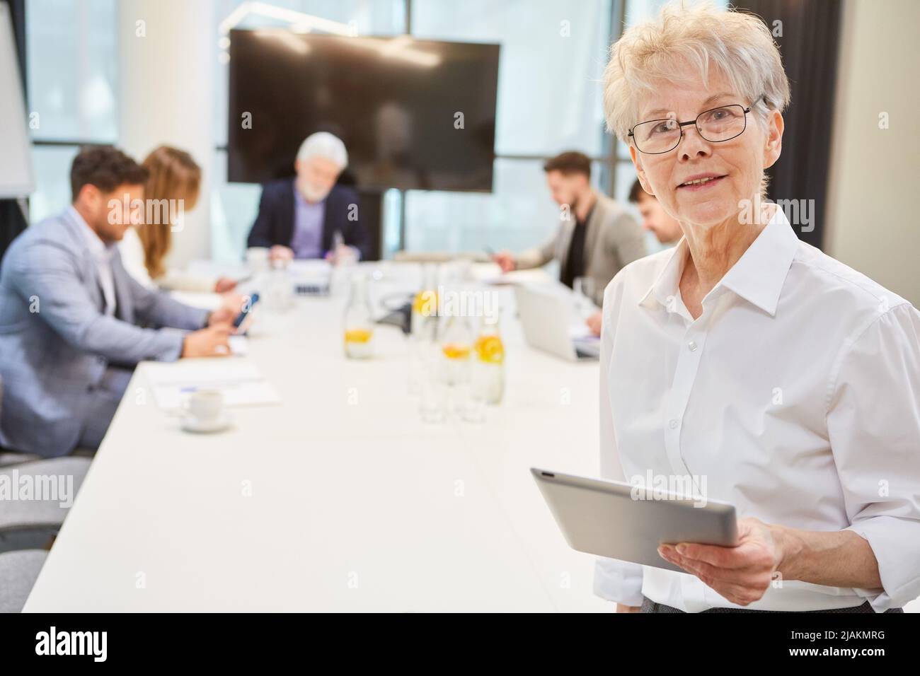 Fidata donna d'affari come capo che usa tablet pc in riunione con il team in background Foto Stock