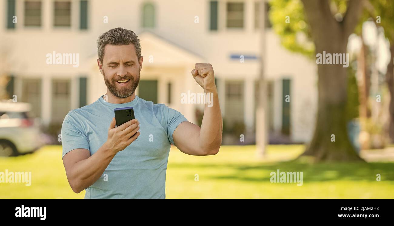 uomo maturo felice in piedi all'aperto a casa lettura messaggio su smartphone, immobiliare Foto Stock