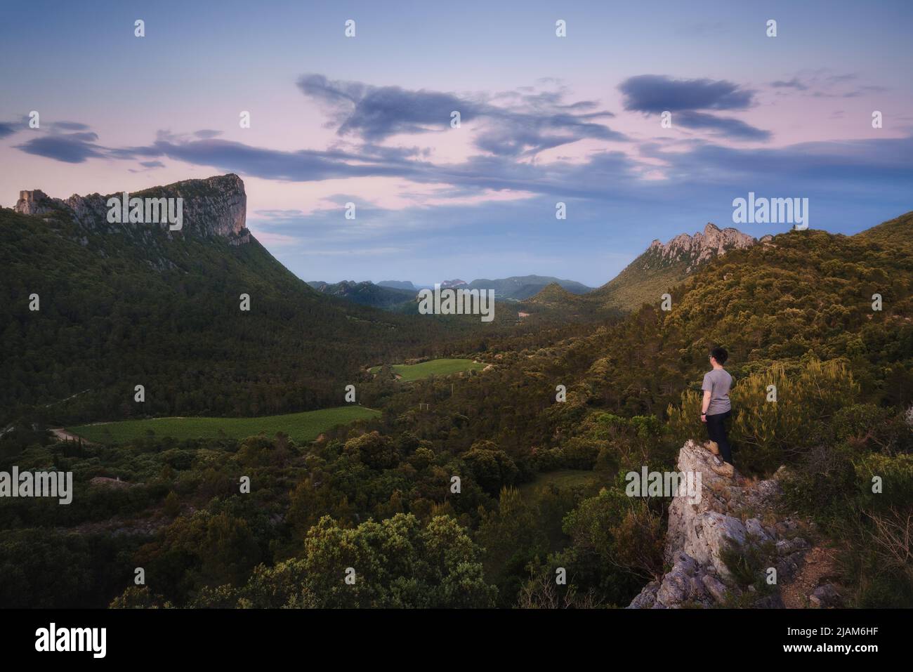 Un uomo che si erge sul bordo della scogliera, si affaccia sul Pic Saint-Loup e Pic de l'Hortus, due famose montagne nella Fance meridionale Foto Stock