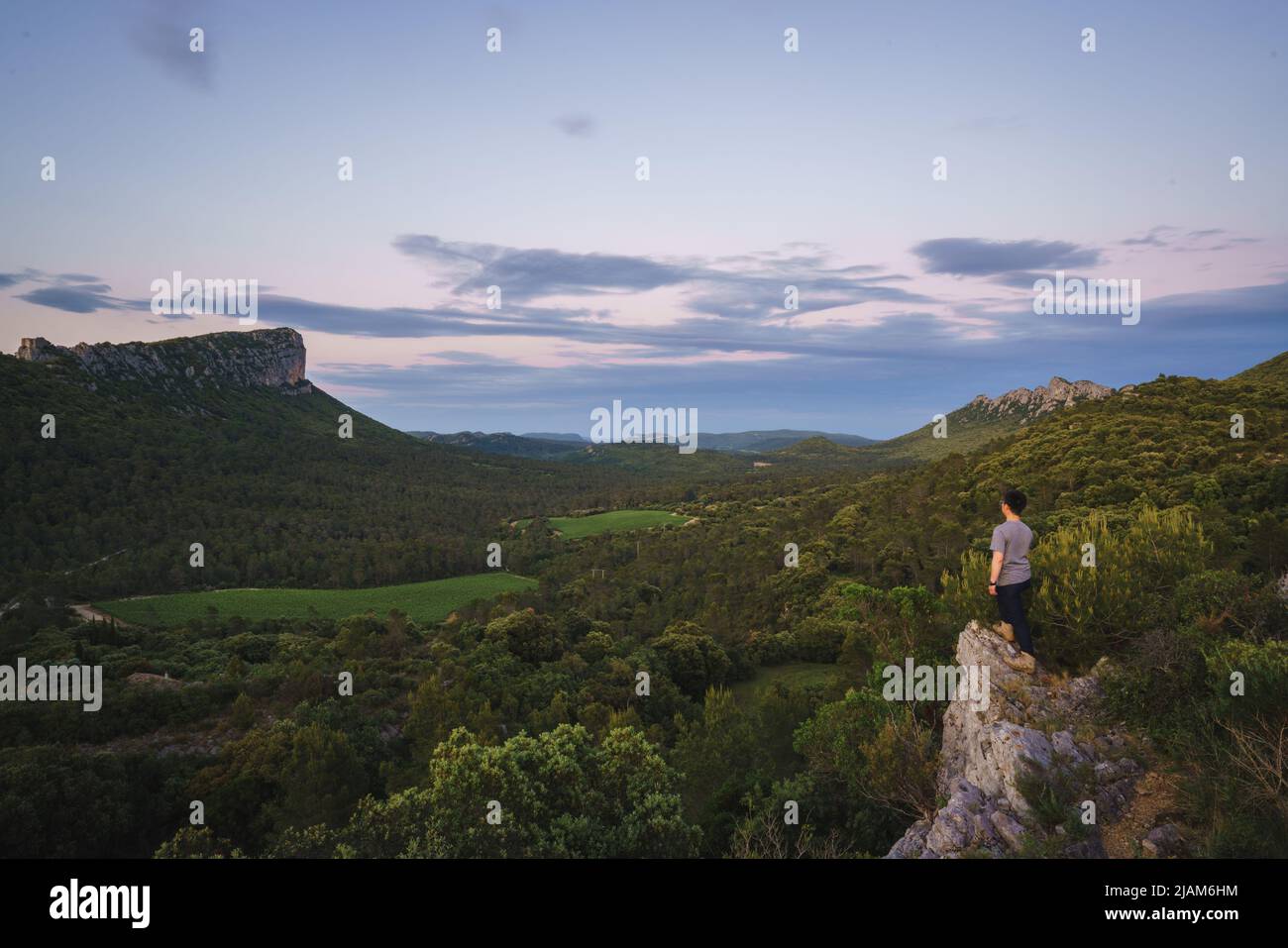 Un uomo che si erge sul bordo della scogliera, si affaccia sul Pic Saint-Loup e Pic de l'Hortus, due famose montagne nella Fance meridionale Foto Stock