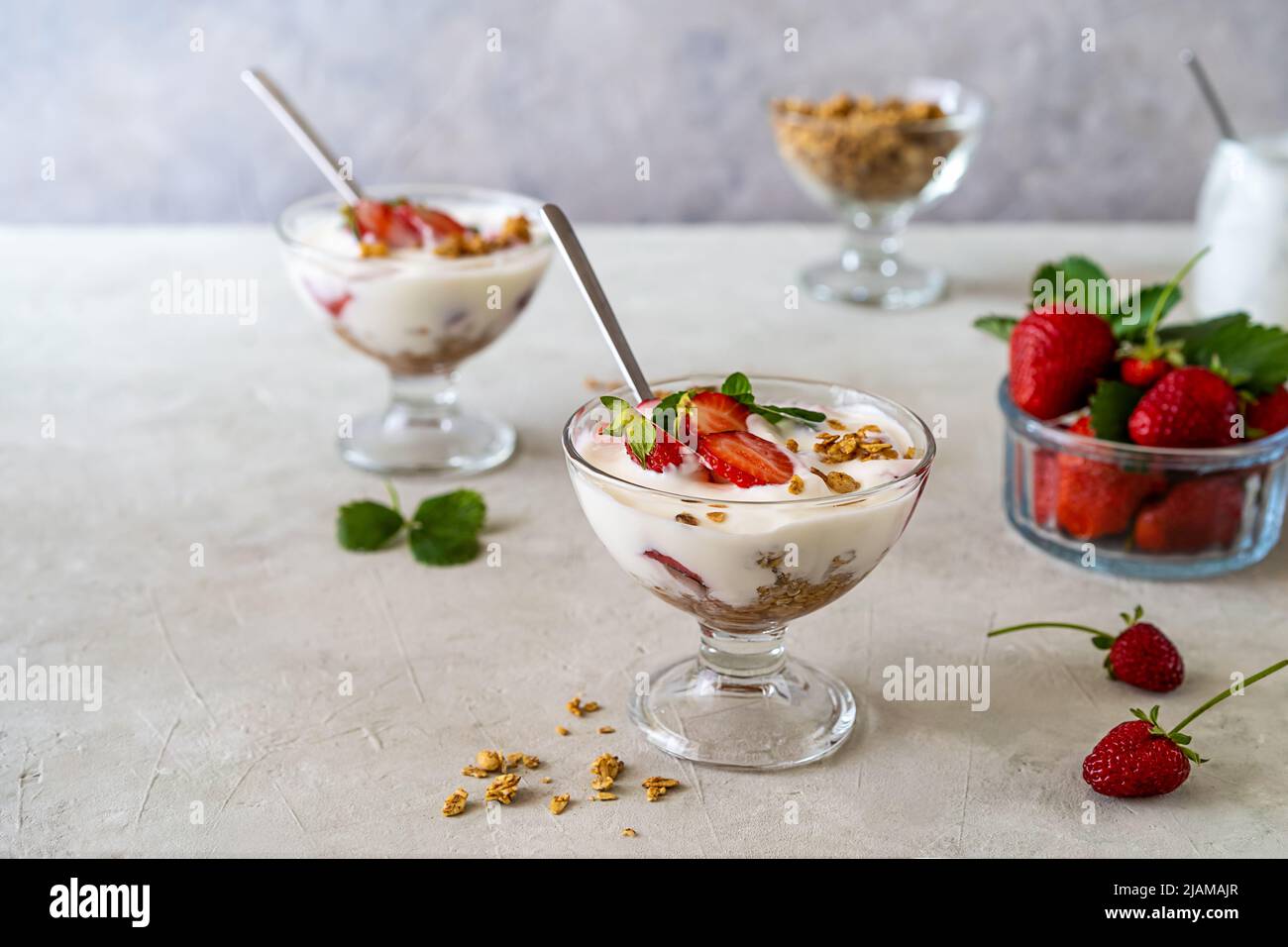 Yogurt con composto di fragole e granola, con frutta fresca in tazze da dessert su sfondo grigio. Spazio di copia Foto Stock