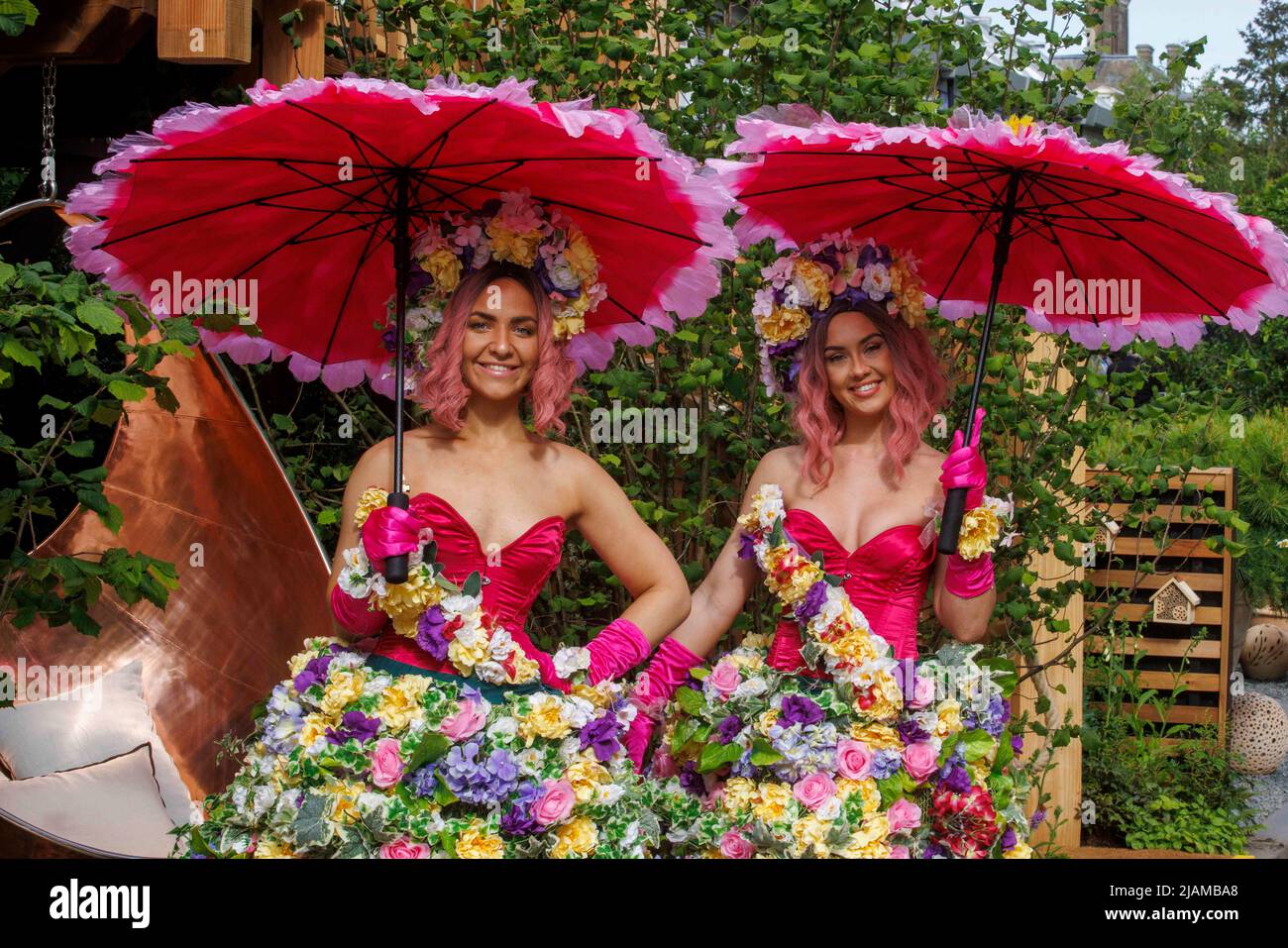 Due modelli che indossano abiti e ghirlande floreali e che portano ombrelloni colorati al Salone dei Fiori RHS Chelsea. Foto Stock