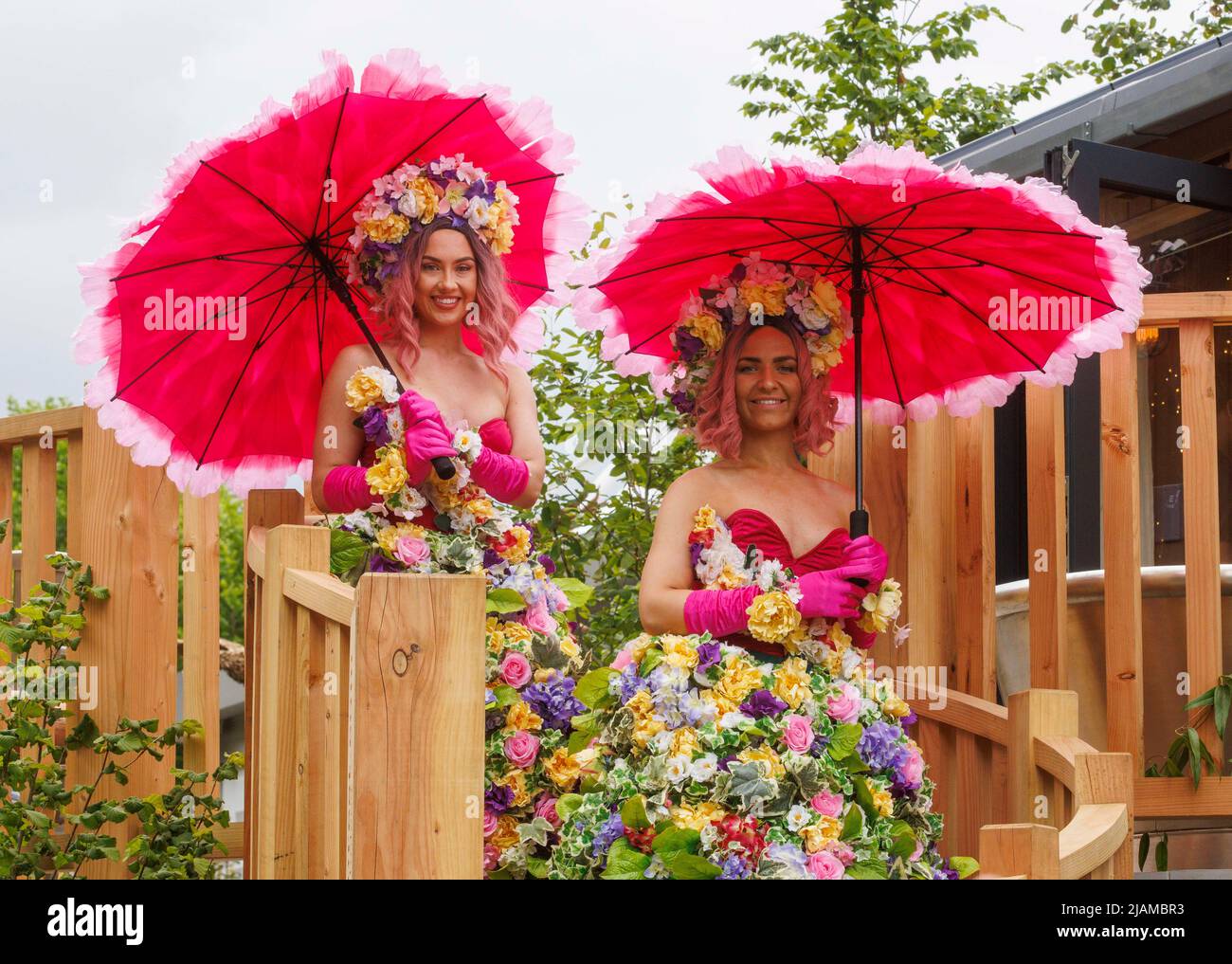 Due modelli che indossano abiti e ghirlande floreali e che portano ombrelloni colorati al Salone dei Fiori RHS Chelsea. Foto Stock