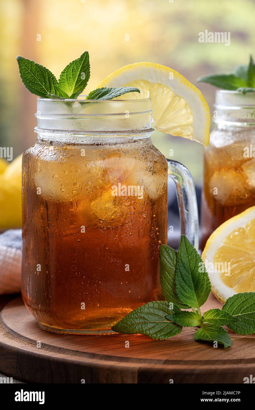 Primo piano di un bicchiere di tè ghiacciato con fetta di limone e menta su un vassoio di legno con sfondo rurale Foto Stock