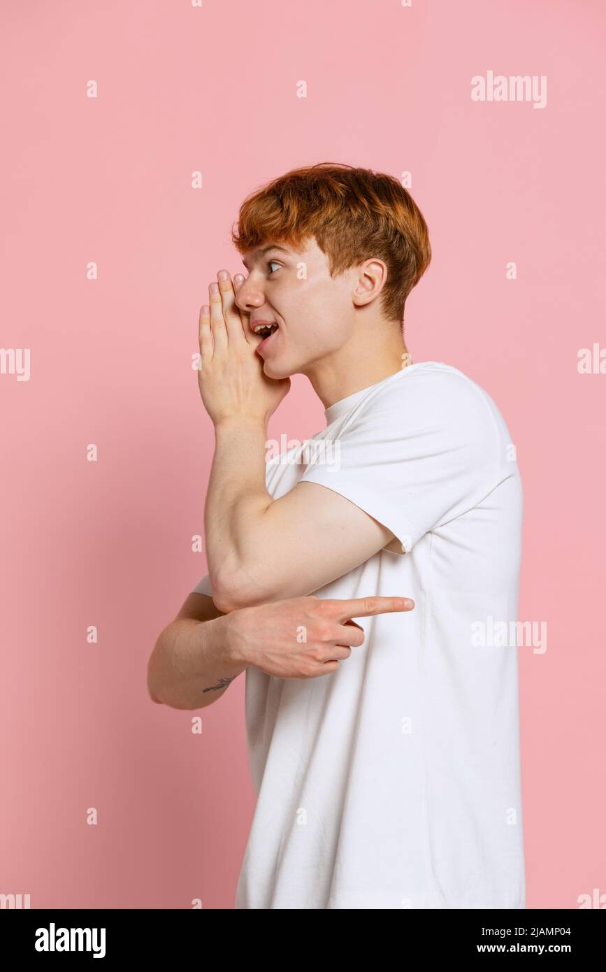 Ritratto di giovane uomo a testa rossa in T-shirt bianca che posa isolato su sfondo rosa studio. Concetto di gioventù, moda, emozioni, espressione facciale Foto Stock