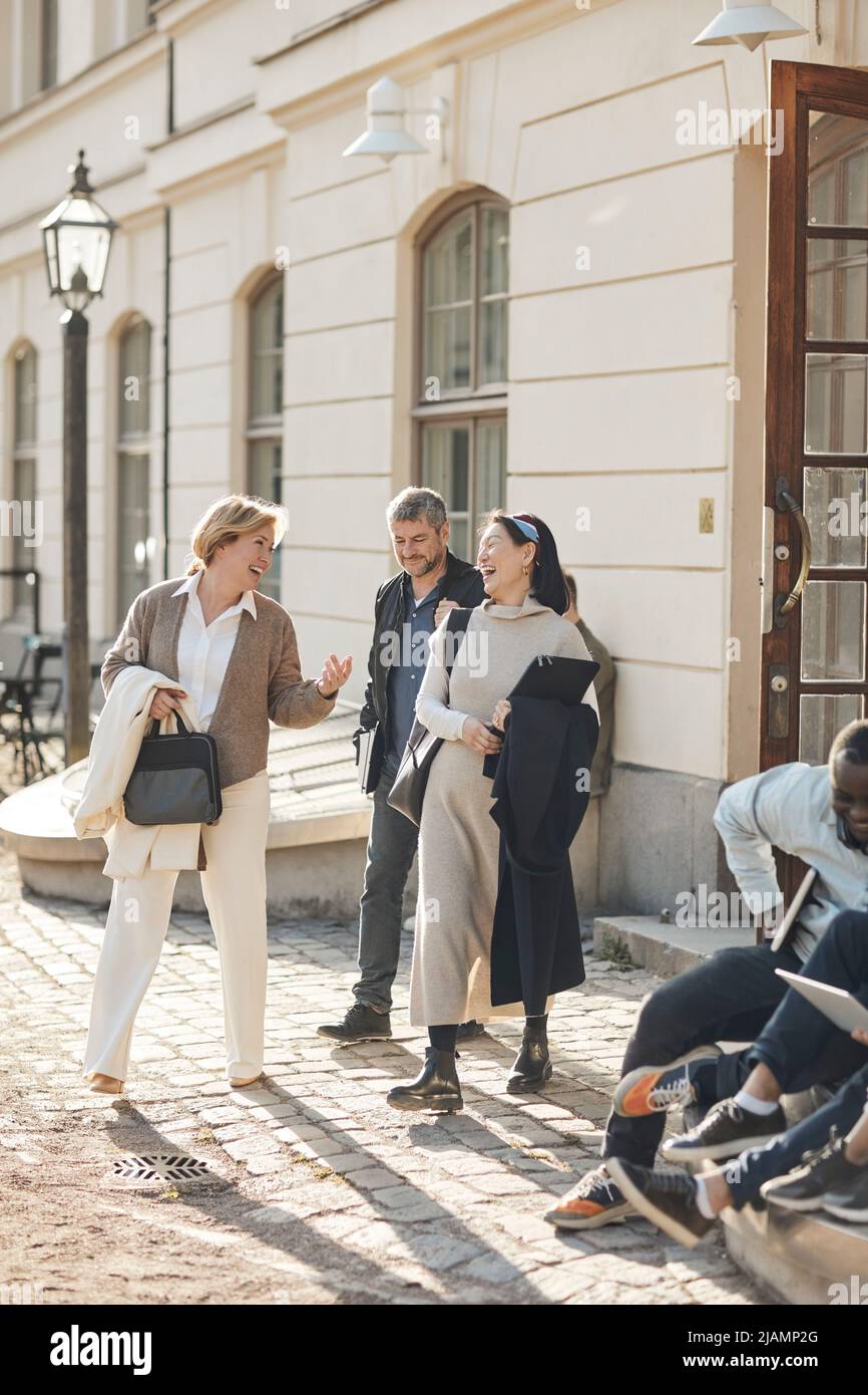 Professori allegri di sesso maschile e femminile che parlano tra loro mentre si parte dalla costruzione universitaria Foto Stock