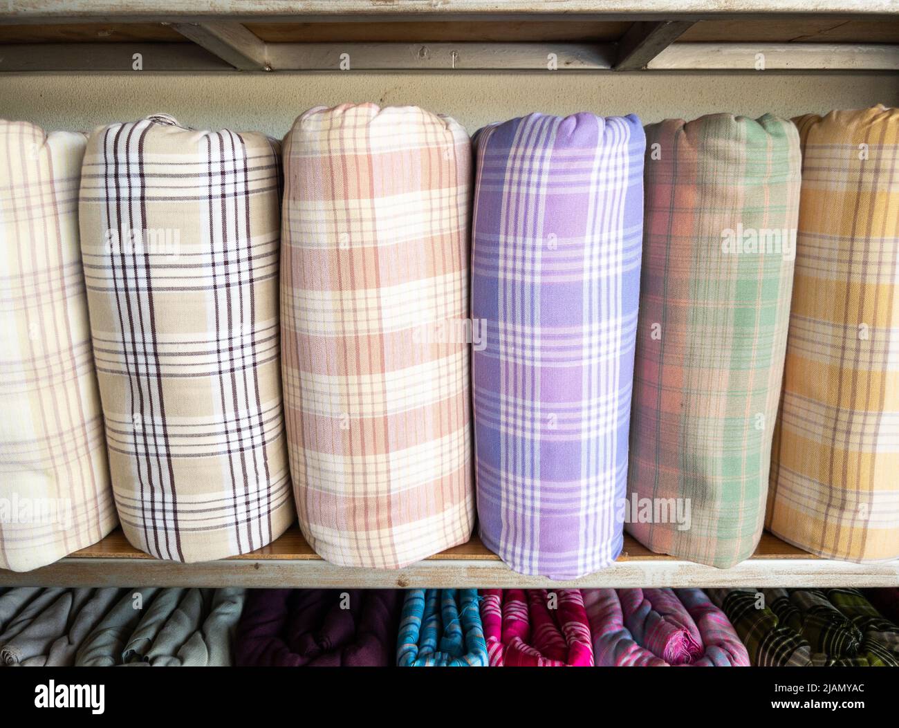 I rotoli di seta fatti a mano con il motivo a plaid sono su scaffali all'interno di un negozio di abbigliamento locale in Thailandia, vista frontale con lo spazio copia. Foto Stock