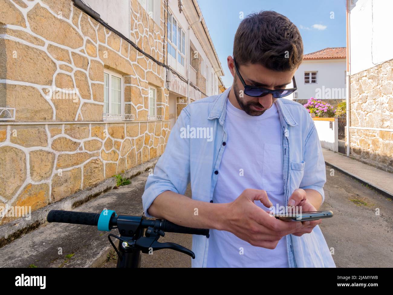 Giovane uomo in abiti casual accanto a uno scooter elettrico mentre guarda il suo smartphone Foto Stock