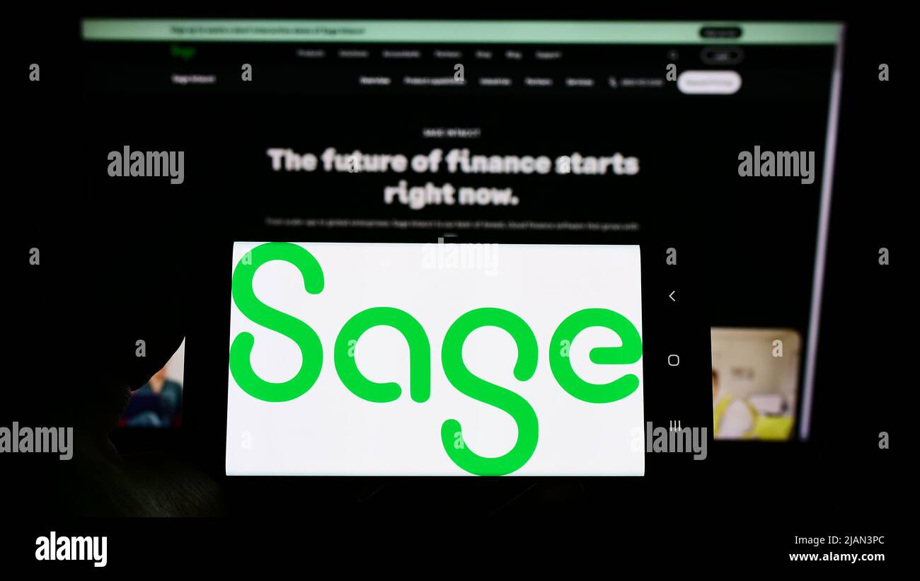 Persona che detiene smartphone con il logo della società di software britannica The Sage Group plc sullo schermo di fronte al sito web. Mettere a fuoco il display del telefono. Foto Stock