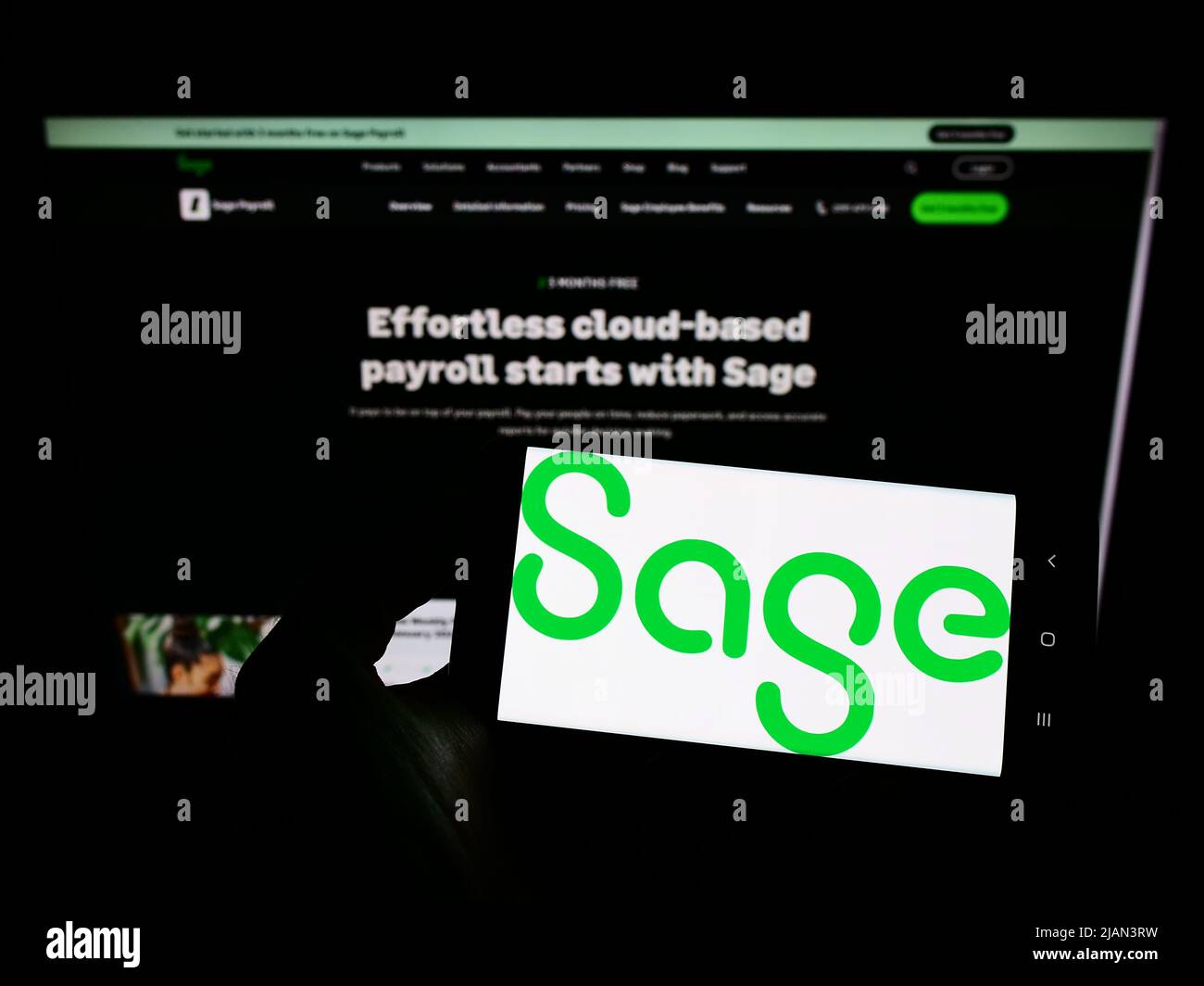 Persona che tiene il cellulare con il logo della società di software britannica The Sage Group plc sullo schermo di fronte al sito web aziendale. Mettere a fuoco sul display del telefono. Foto Stock
