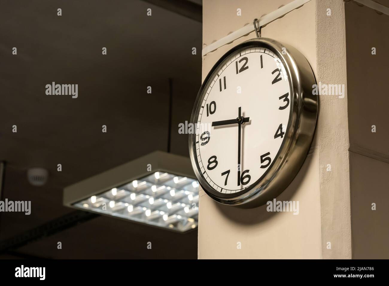 Un singolo orologio industriale semplice in una sala di fabbrica o in un ufficio aziendale a parete. Lavoro da 9 a 5, orari di entrata e uscita, flusso di tempo, salario orario ab Foto Stock