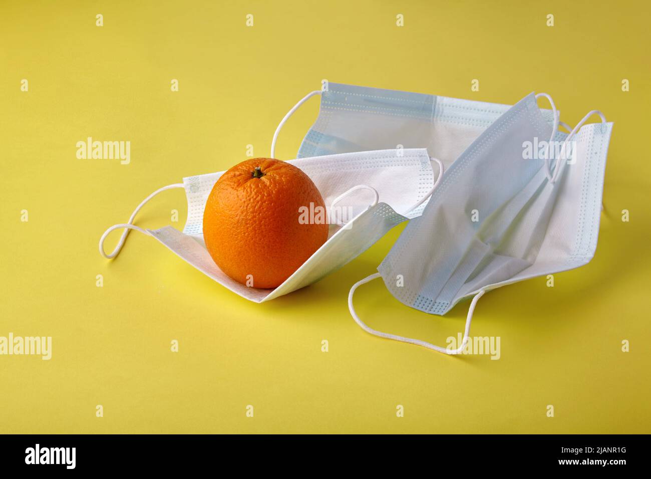 Un arancione fresco giace sulle maschere mediche su uno sfondo giallo. Influenza stagionale freddo allergie protezione Foto Stock