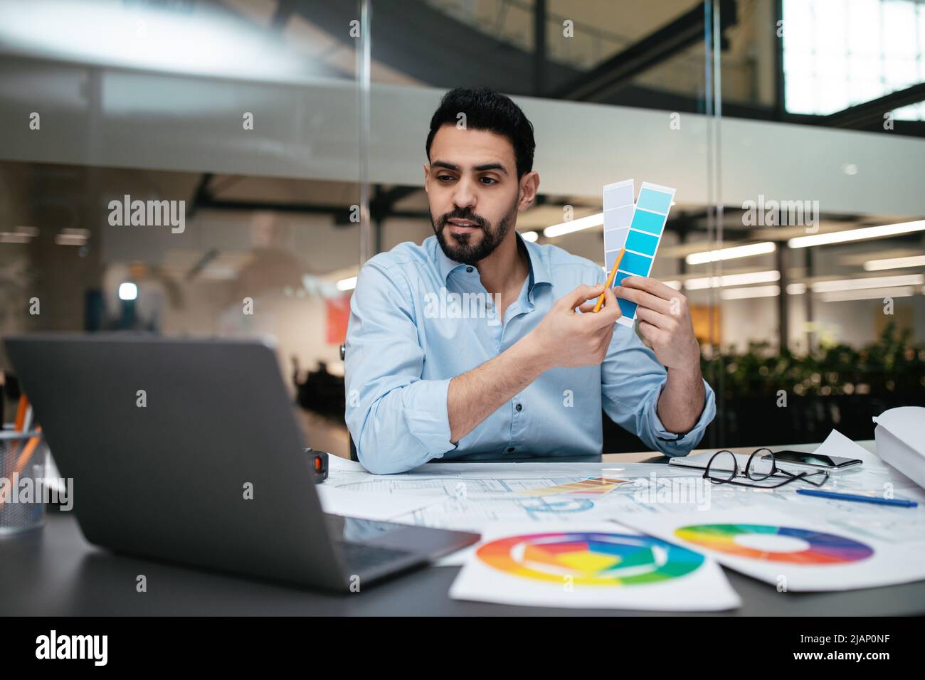 Concentrato giovane e bello uomo arabo ingegnere designer con barba mostra le tavolozze di colore in laptop Foto Stock