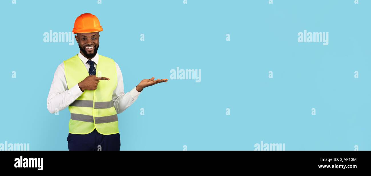 Bella offerta. Sorridente tecnico di costruzioni nere che punta al suo palmo vuoto Foto Stock