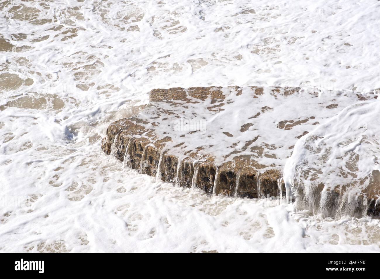 Acqua che si spillano dalla base di un groyne di difesa del mare sulla spiaggia di Brighton, Sussex orientale, Inghilterra, Regno Unito Foto Stock
