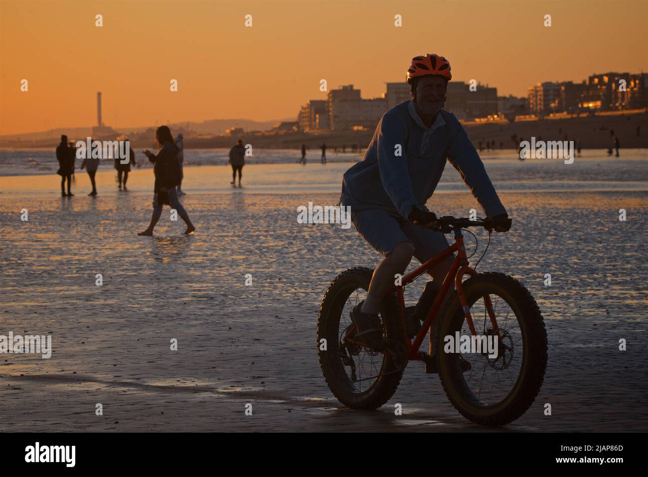 Forme di persone in spiaggia con bassa marea, tra cui un ciclista in primo piano. Brighton & Hove, East Sussex, Inghilterra, Regno Unito. Foto Stock