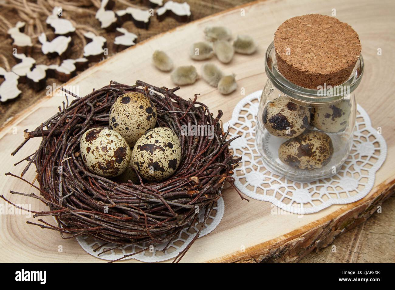 Uova di uccello in un nido, uova in un vaso, lepri di legno e germogli di salice su una sega di legno. Concetto di Pasqua Foto Stock
