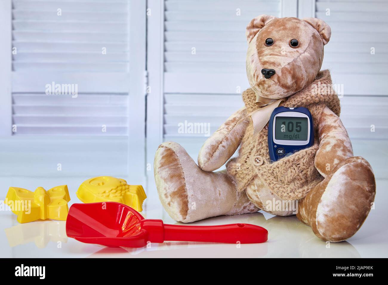 Orsacchiotto con un glucometro di sangue e giocattoli sparsi per bambini su sfondo blu. Il concetto di trattamento del diabete mellito nei bambini, hype Foto Stock