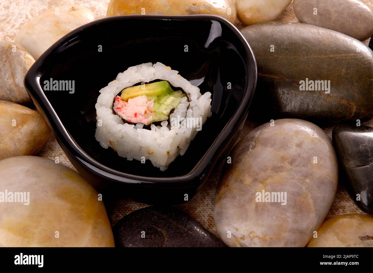 Un singolo pezzo di sushi californiano, esposto artfully su pietre lisce in un piccolo piatto nero Foto Stock