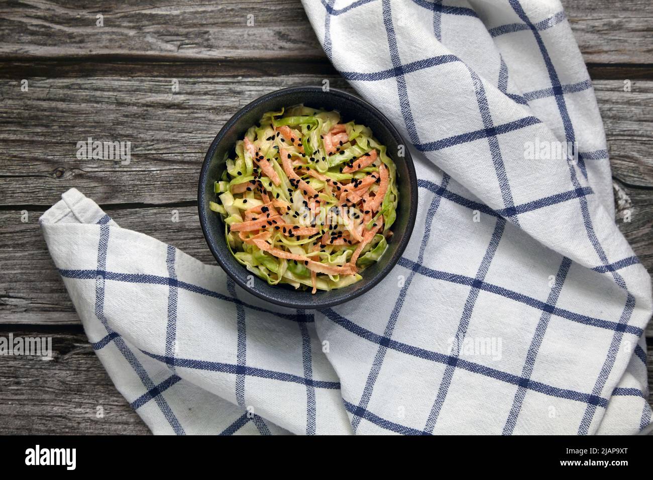 Insalata di cavolo bianco e carota con semi neri di cumino e maionese e condimento al limone in una ciotola di ceramica nera su un vecchio sfondo di legno. Foto Stock