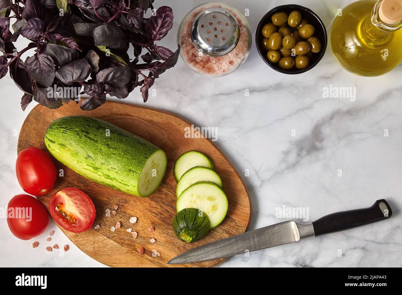 Pomodori zucchini olive olio di basilico e sale su tavola di legno su tavola leggera. Ingredienti per preparare pasti vegetariani Foto Stock
