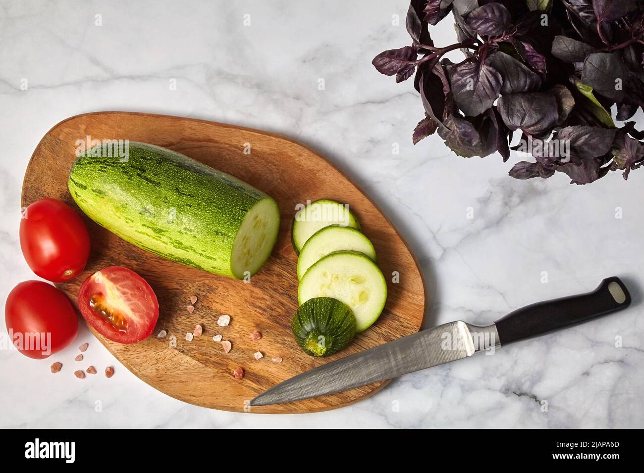 Zucchine, pomodori e basilico su un tavolo di legno su un tavolo leggero. Ingredienti per preparare pasti vegetariani Foto Stock