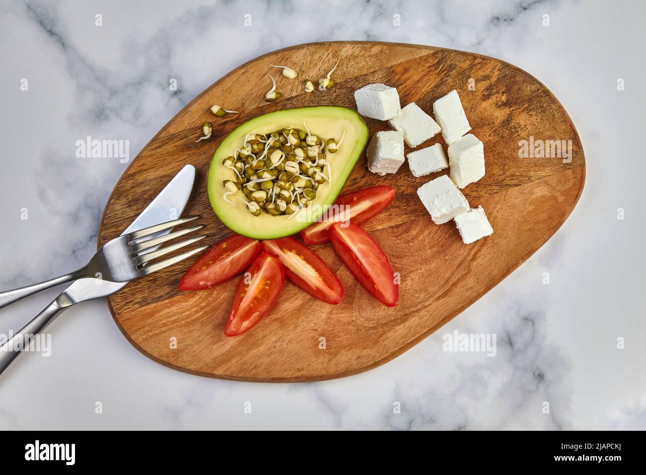 Avocado germogli mungo fagiolo pomodori cagliata e posate su un asse di legno su un tavolo leggero. Vista dall'alto Foto Stock