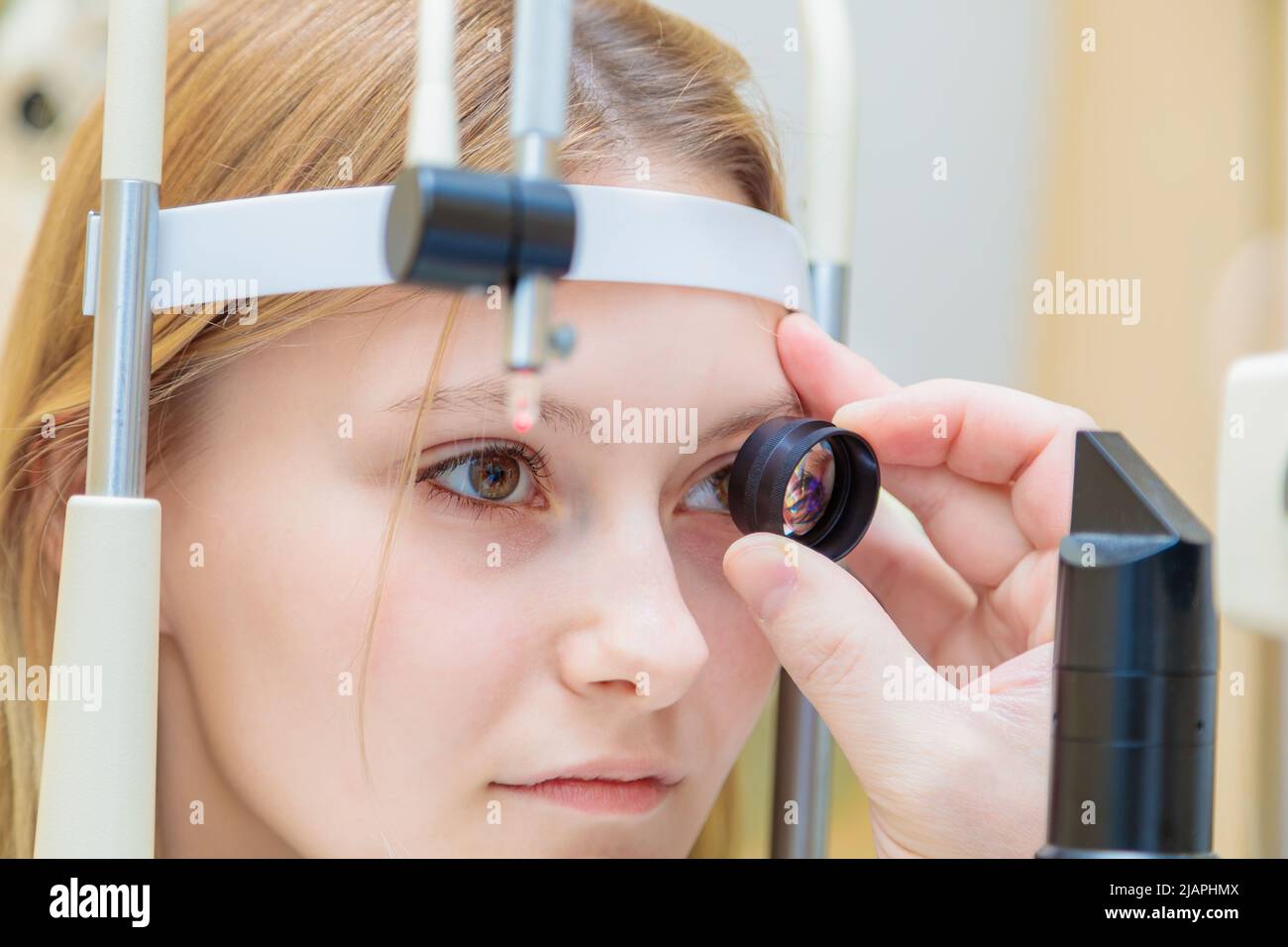 Un oftalmologo maschile controlla la vista di una giovane ragazza utilizzando un dispositivo moderno con un fascio di luce. Foto Stock