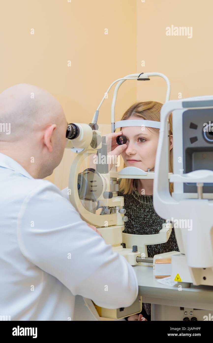 Un oftalmologo maschile controlla la vista di una giovane ragazza utilizzando un dispositivo moderno con un fascio di luce. Foto Stock