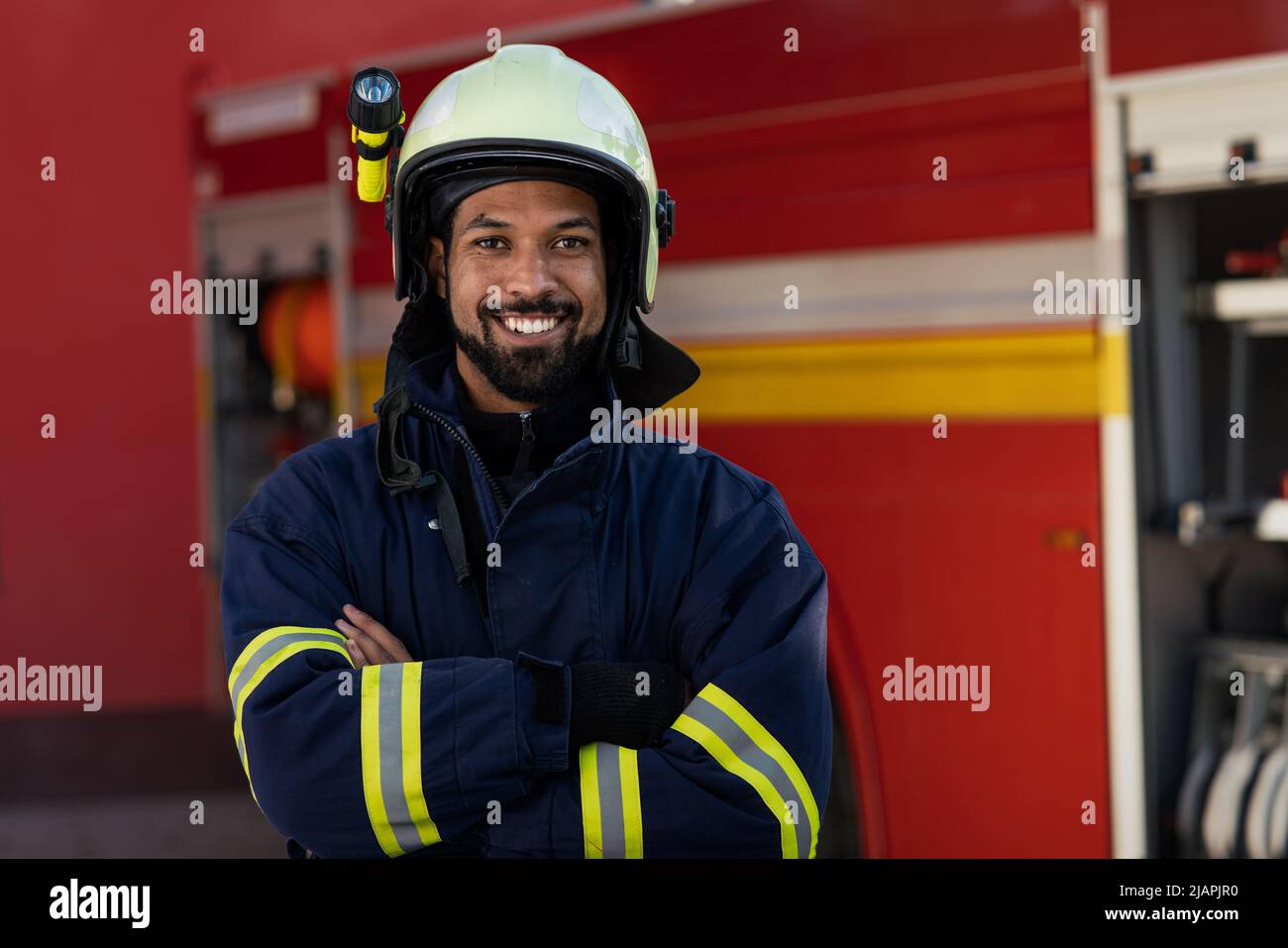 Felice giovane afro-americano vigile del fuoco con camion del fuoco in background. Foto Stock